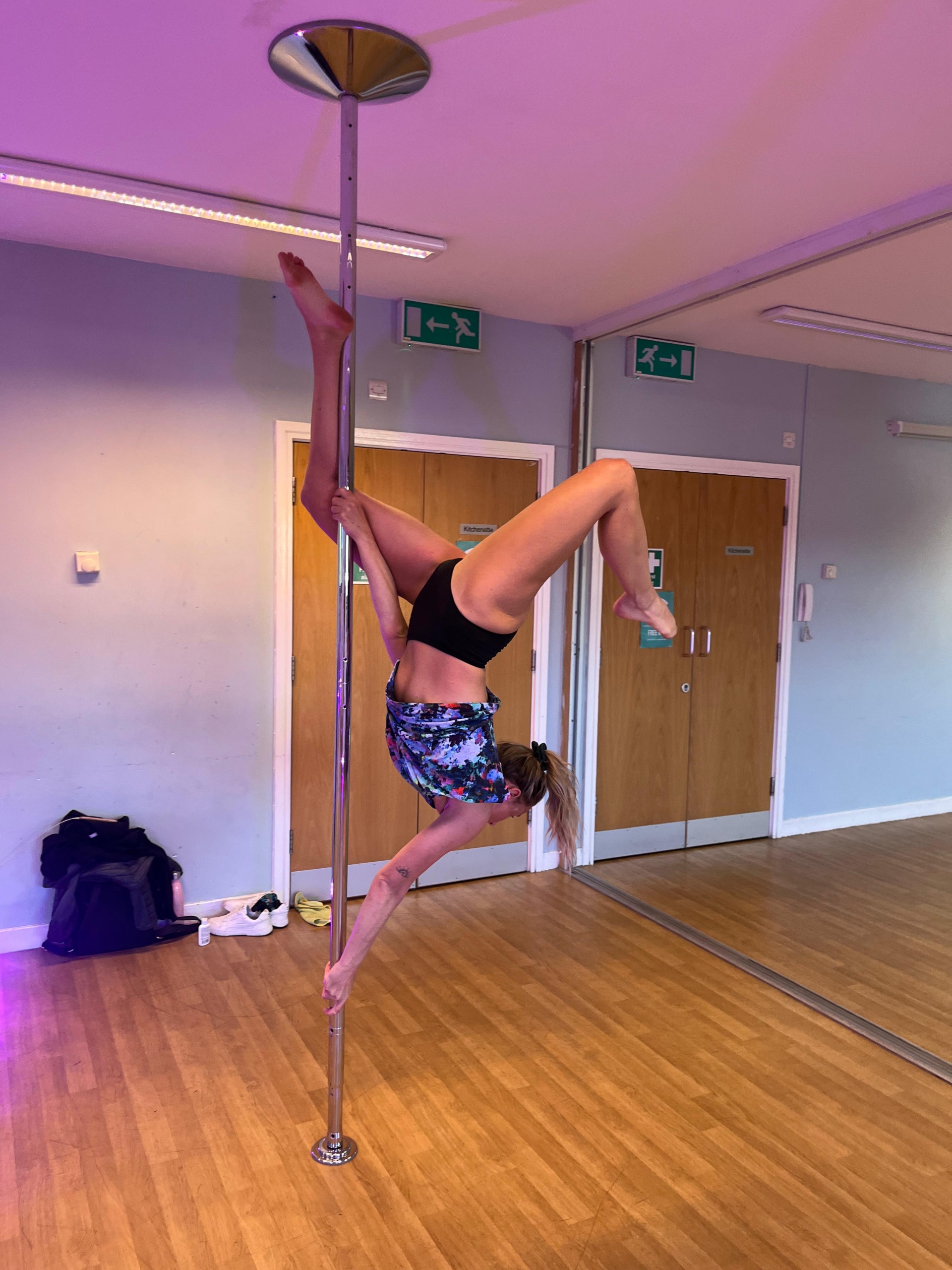 Upside down and elevated women on a pole dancing pole holding on with two hands and her right leg upside down.